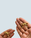 Hand-held display of gold-tone silk bow stud earrings showing premium finish - Trinketly BD