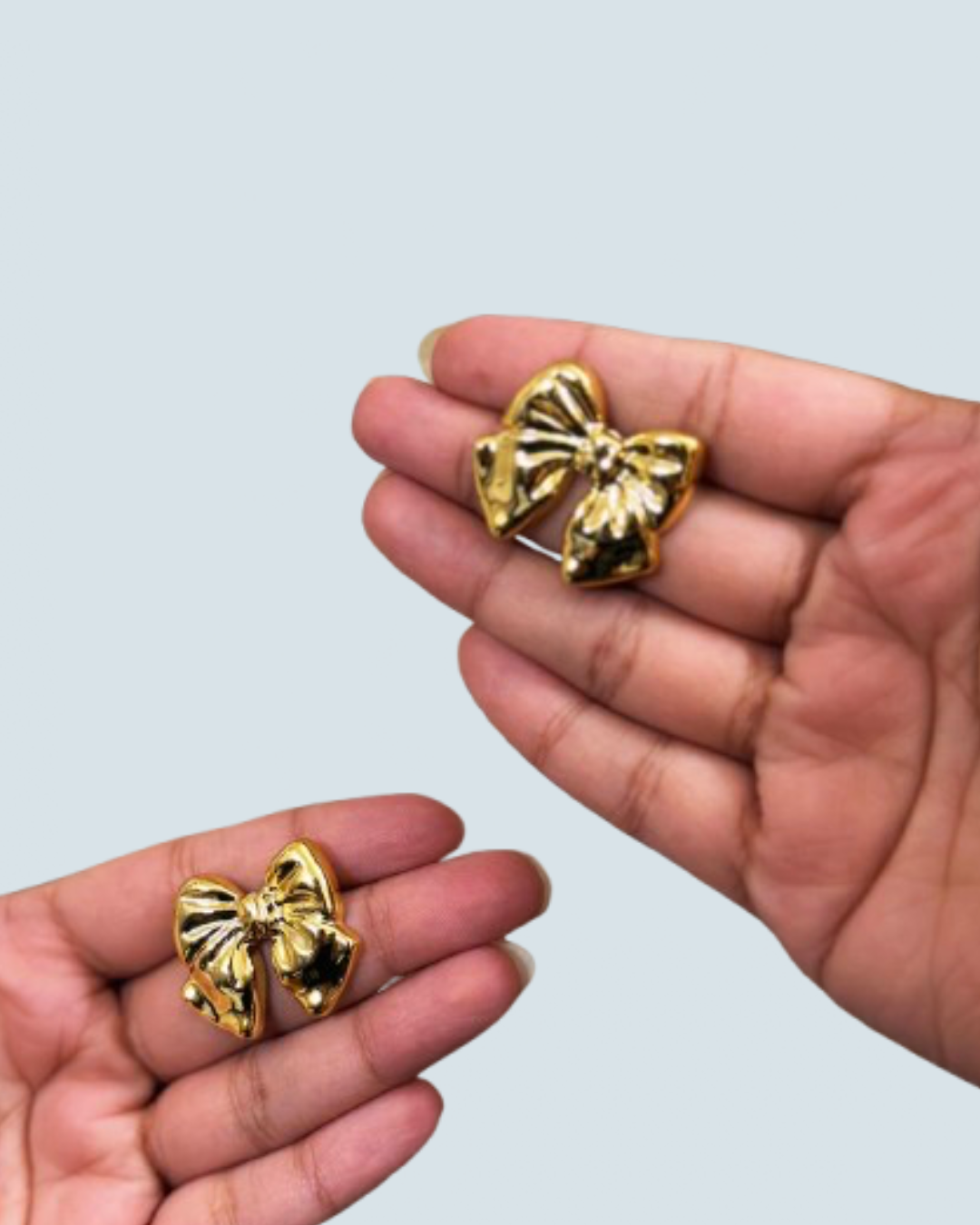 Small bow bloom gold-tone stud earrings shown in hand - Trinketly BD
