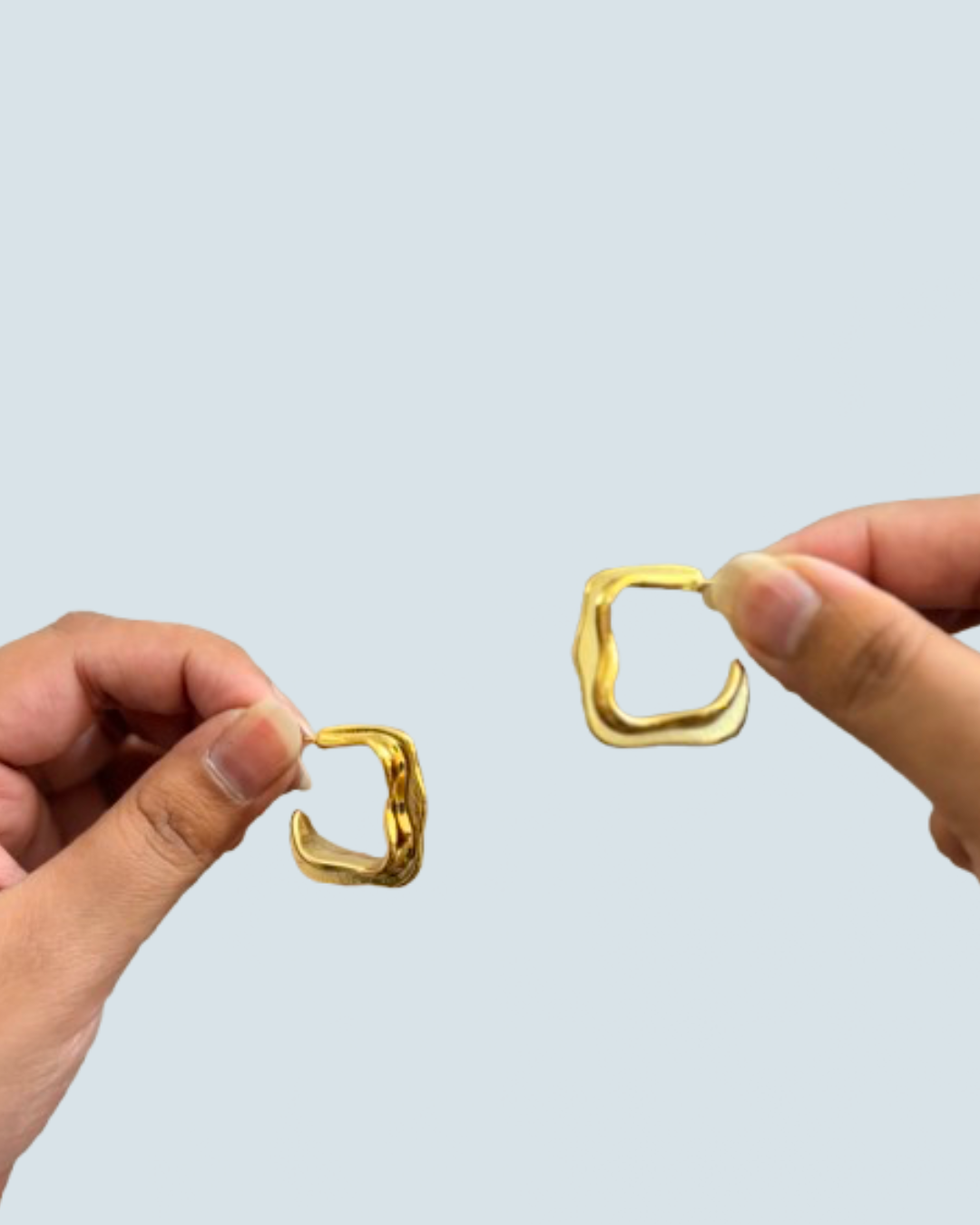 Hand-held view of fluid wave gold-tone hoop earrings for modern evening style - Trinketly BD